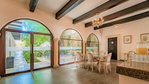 Un'ampia sala da pranzo con pavimento in legno, un lampadario e vista sul patio esterno attraverso grandi vetrate.