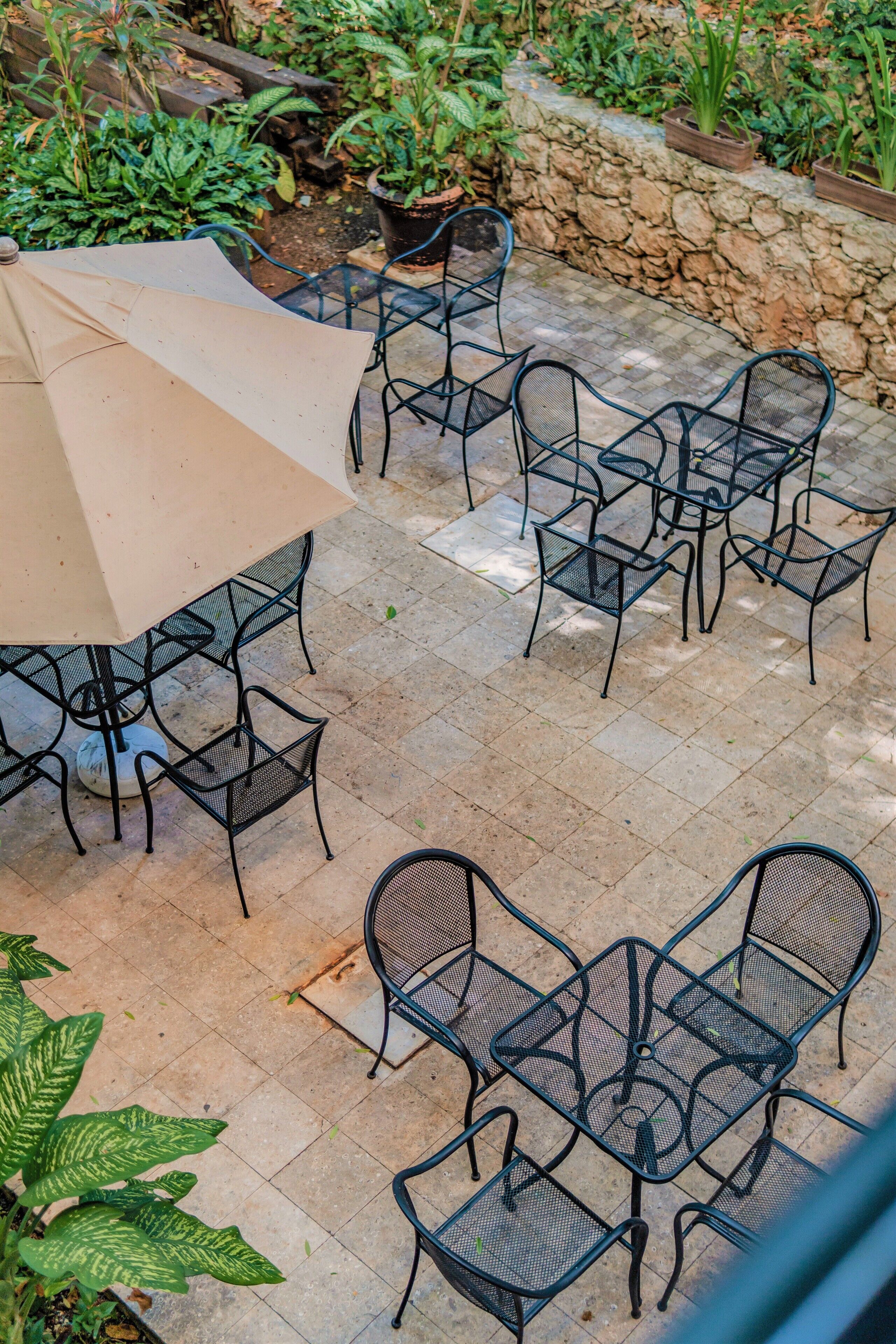 An outdoor patio with metal chairs and tables, surrounded by a stone wall and potted plants.