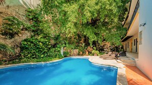 Una piscina circondata da vegetazione lussureggiante, con un solarium e lettini.