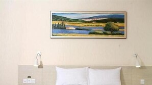 A hotel room with a bed, two bedside lamps, and a framed landscape painting on the wall. - Hanting Express Dandong Train Station (Dandong)