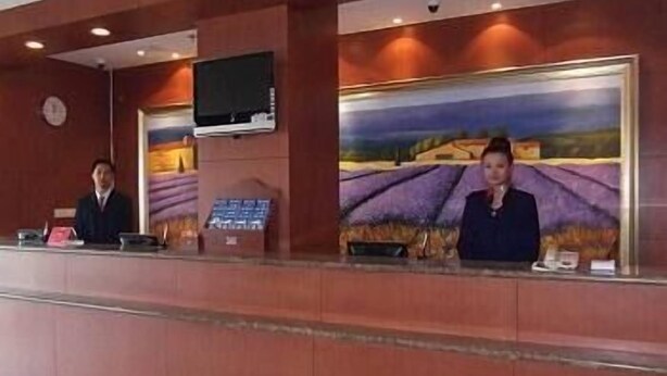 A reception desk with two staff members, a clock, and a painting of a landscape. - Hanting Express Dandong Train Station (Dandong)