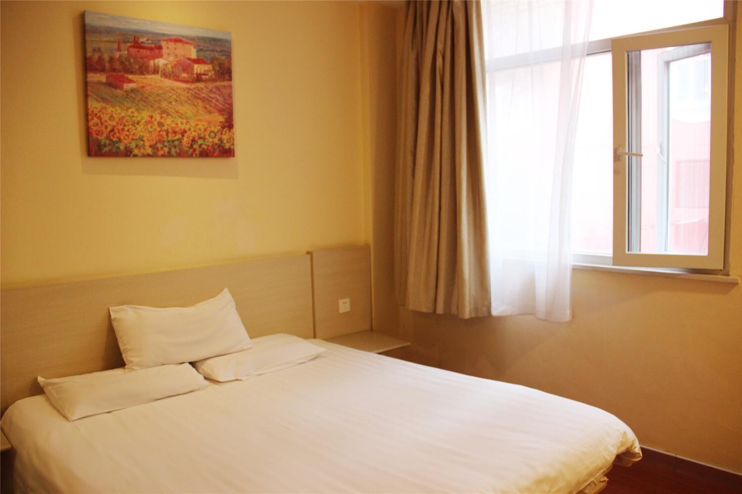 A bedroom with a bed, a painting on the wall, and a window with curtains.
