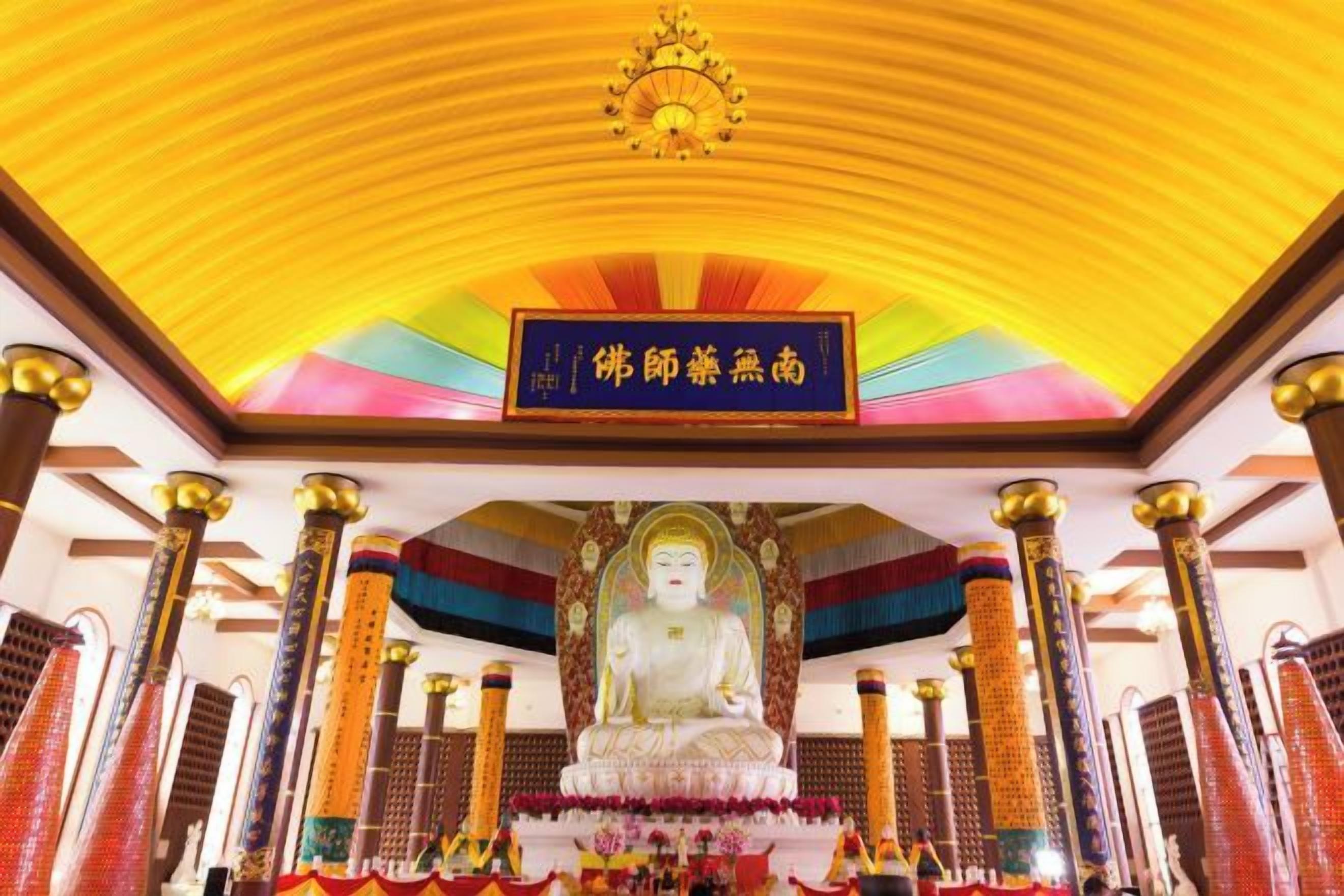 Eine große Statue in einem Tempel mit farbenfroher Decke und traditionellen Säulen.