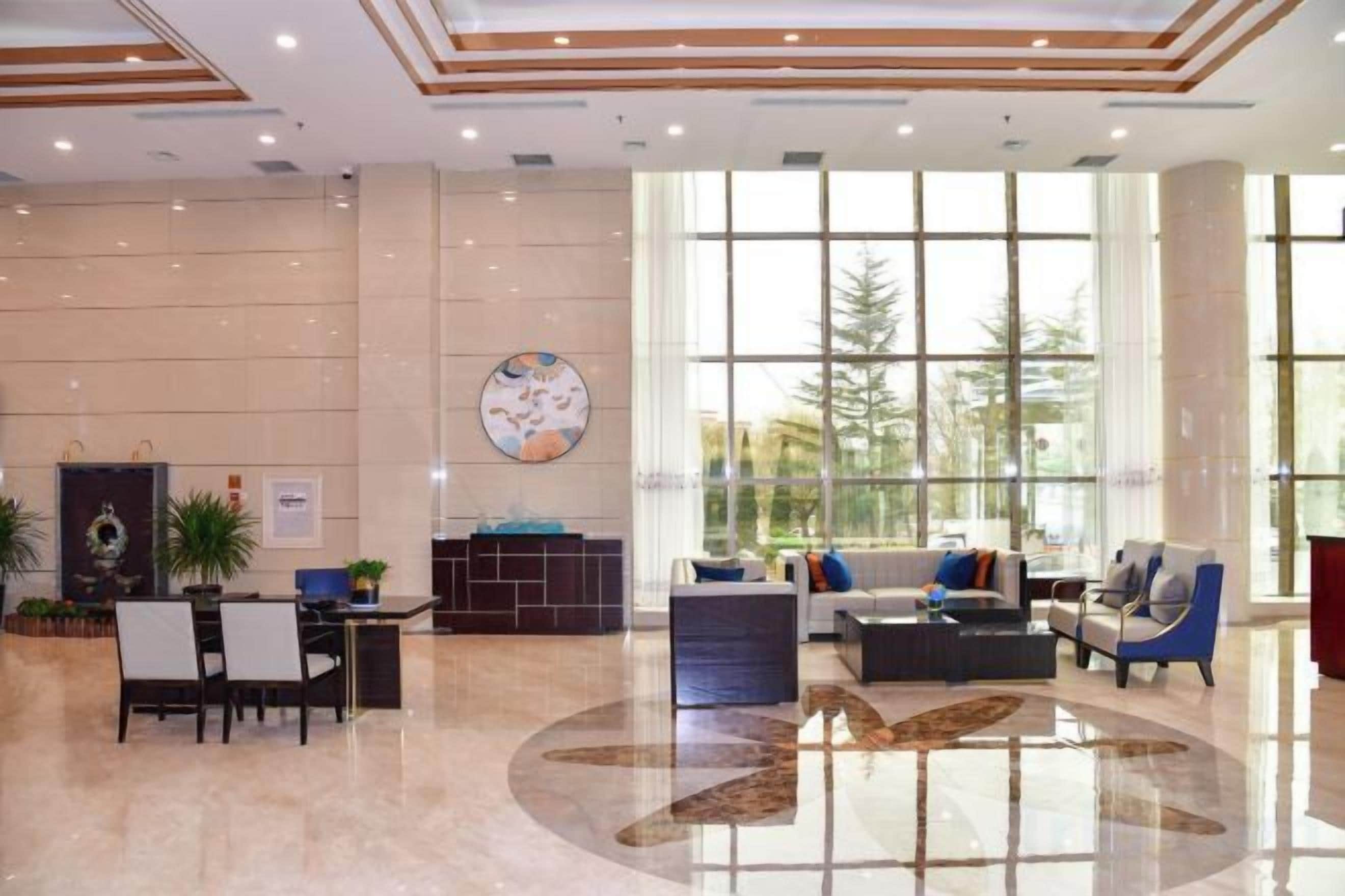 A spacious lobby with a reception desk, seating area, and large windows offering a view of trees.