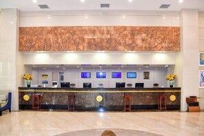 Zona de recepción de un hotel con mostrador de mármol, múltiples monitores y una pared decorativa.