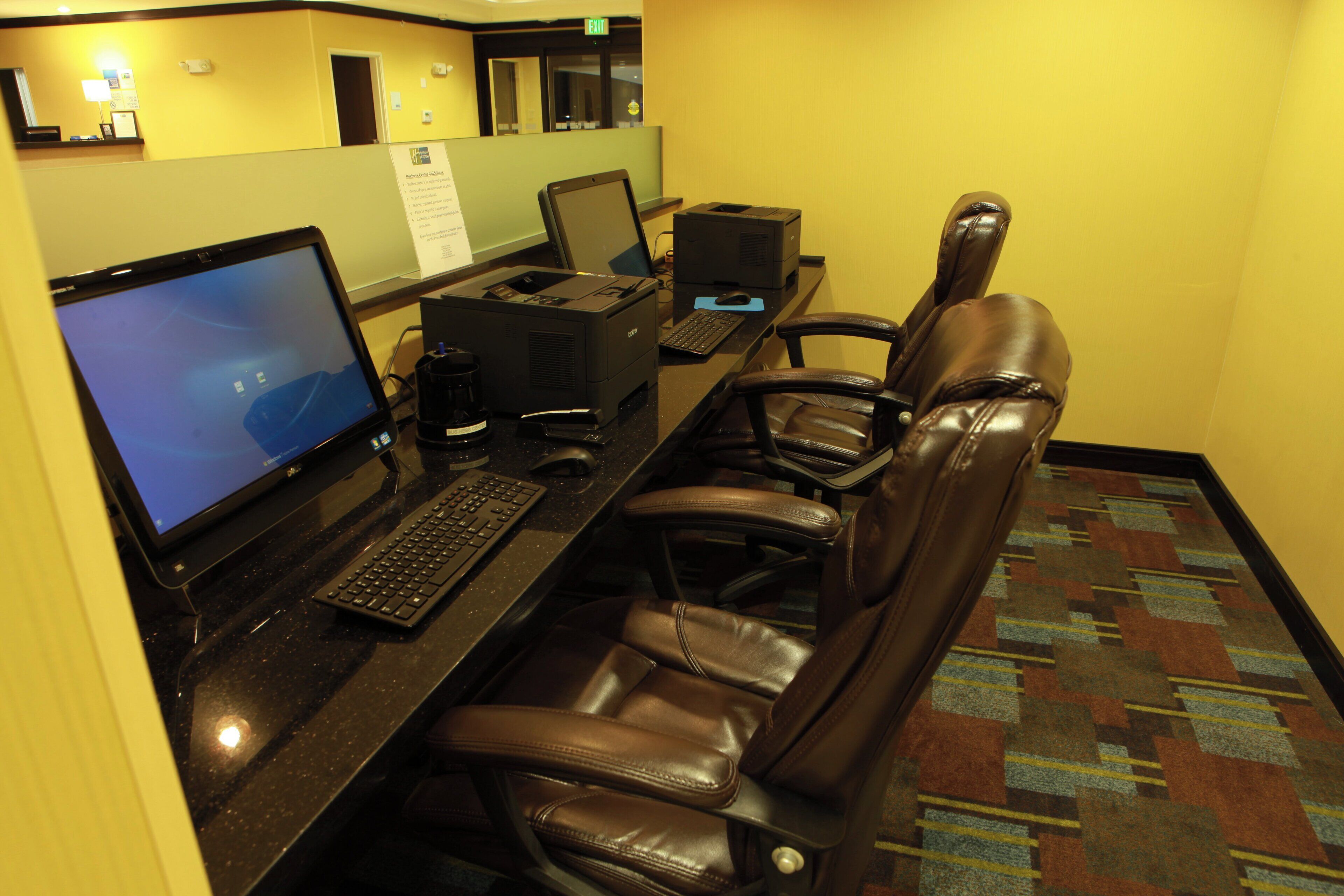 A hotel workspace with a desk, computer, printer, and leather chairs.