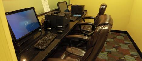 A hotel workspace with a desk, computer, printer, and leather chairs.