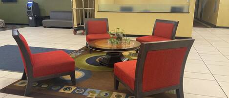 A lobby with a round table, four red chairs, a sofa, a vending machine, and a staircase.