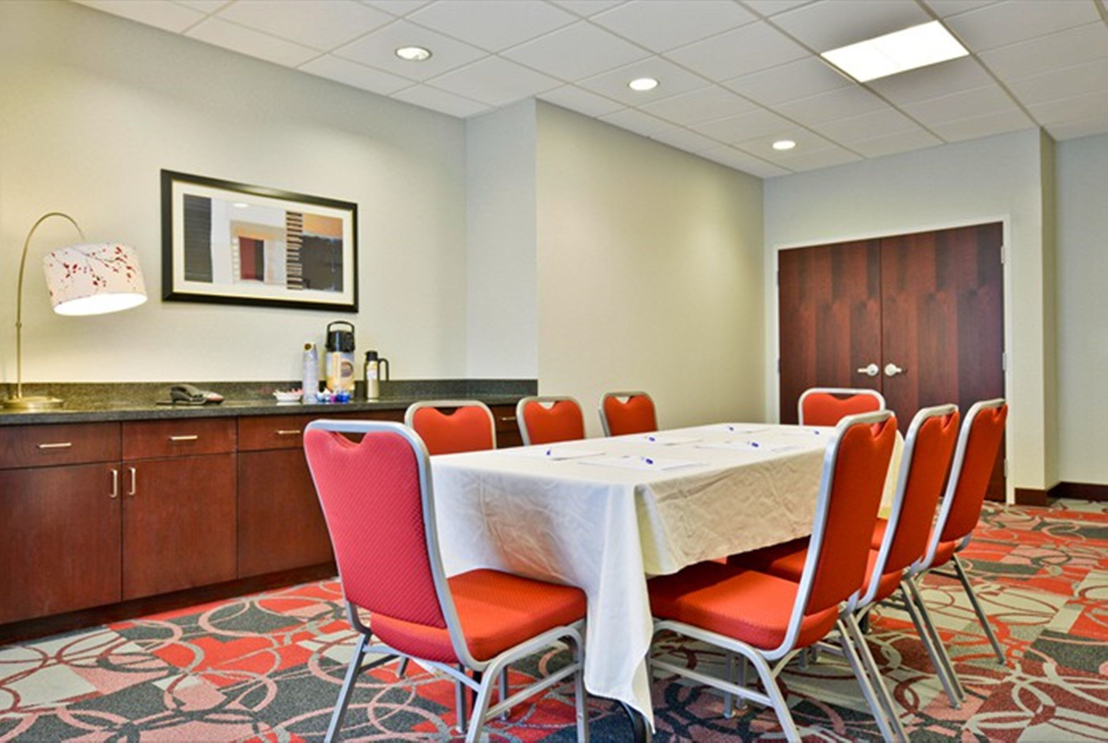 Un salón de conferencias con una mesa, sillas, una kitchenette y una puerta grande de madera.