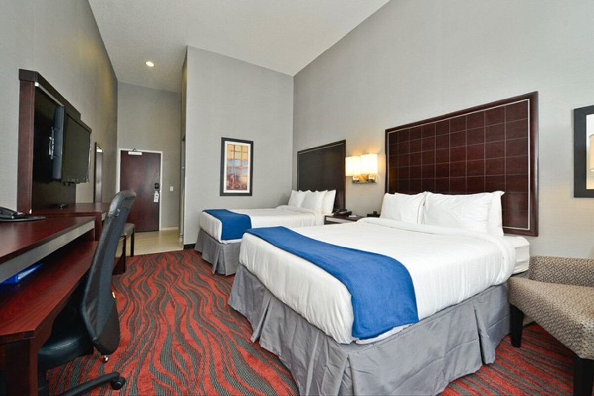 A hotel room with two beds, a desk, a chair, a TV, and a red carpet.