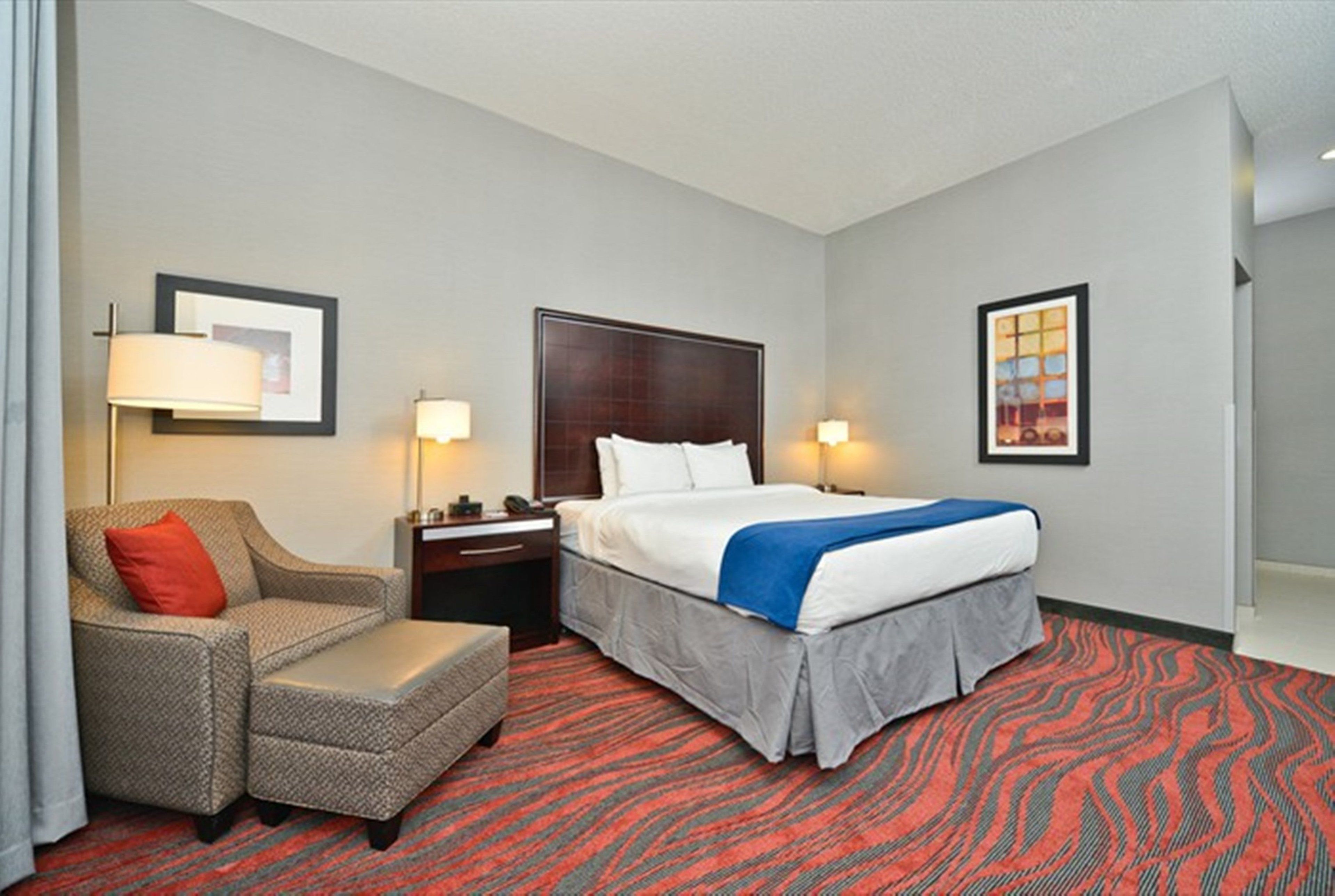 A hotel room with a bed, a chair, a nightstand, and two wall-mounted lamps.