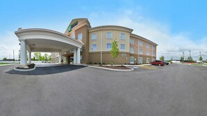 A hotel with a covered entrance, a landscaped area with small trees, and a clear sky.