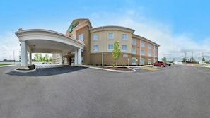 A hotel with a covered entrance, a landscaped area with small trees, and a clear sky. - Holiday Inn Express & Suites Utica by IHG (Utica)