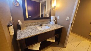Une salle de bain avec un lavabo doté d’un plan de travail en granit, un miroir, un porte-serviettes et un savon Dove.