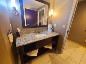 A bathroom with a granite countertop sink, a mirror, a towel rack, and a bottle of Dove soap. - Holiday Inn Express & Suites Utica by IHG (Utica)