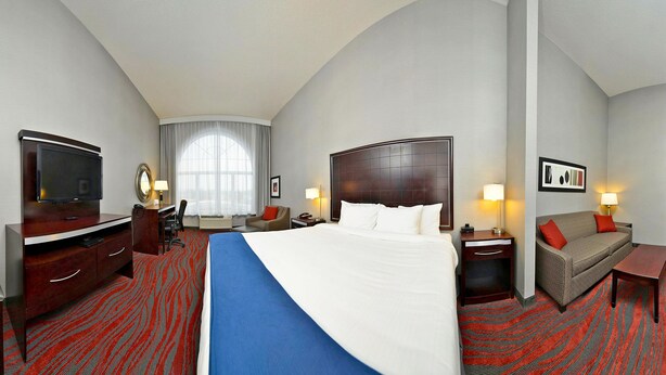 Une chambre d’hôtel avec un grand lit, un bureau avec une chaise, une télévision, un canapé et une fenêtre avec des rideaux.
