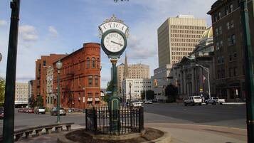 A street scene with a prominent clock tower labeled 'UTICA' in the center, surrounded by a fence and a circular planter.