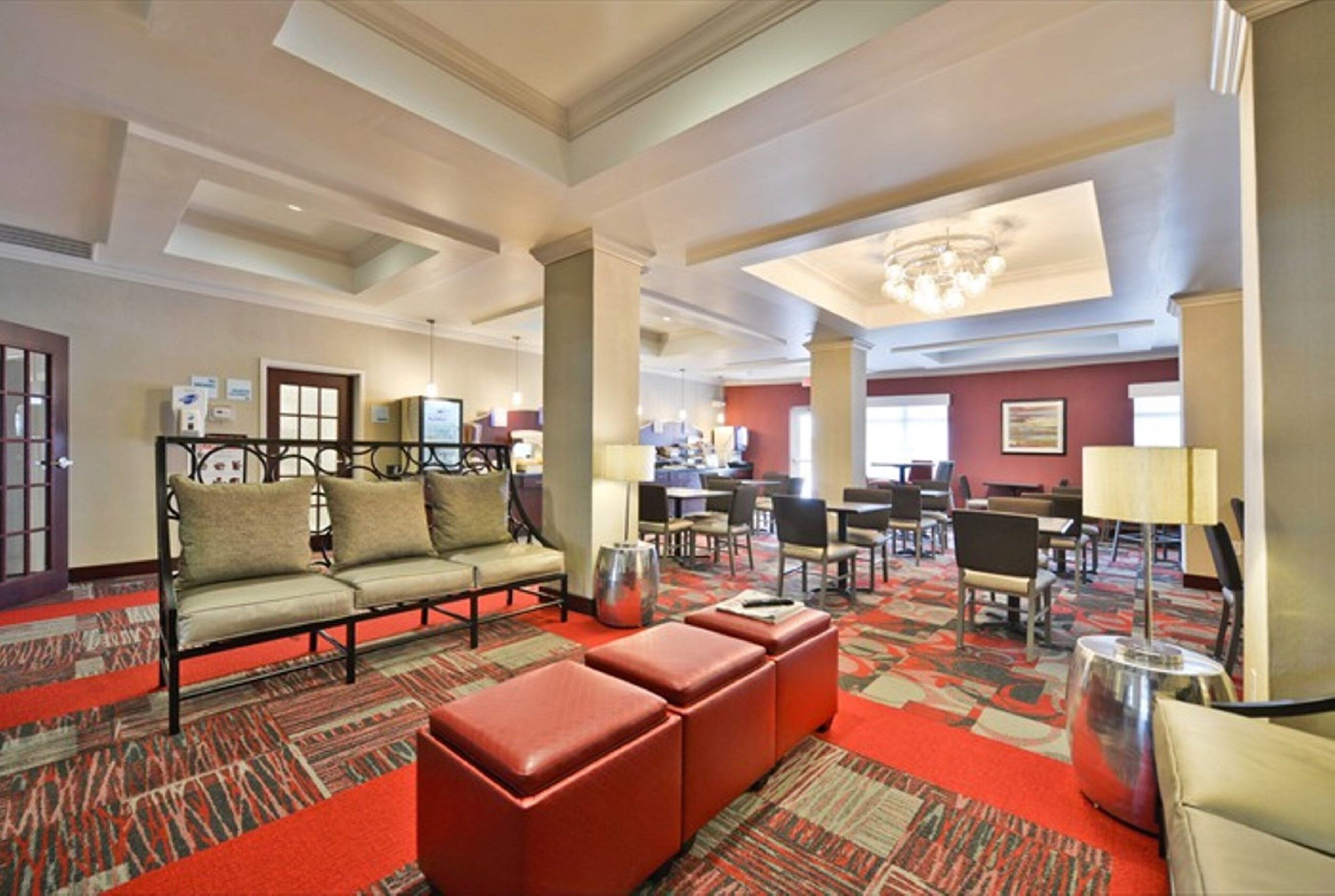 A hotel lobby with a sofa set, a red ottoman, a chandelier, and a patterned carpet.