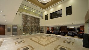 Un vestíbulo amplio con un gran muro decorativo, una zona de estar con sofás de cuero y un candelabro moderno.