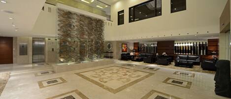 A spacious lobby with a large decorative wall, a seating area with leather sofas, and a modern chandelier.