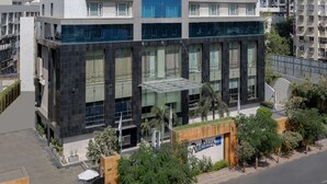 Un hotel moderno de varios pisos con una fachada de vidrio destacada, techo plano y un área de entrada ajardinada.