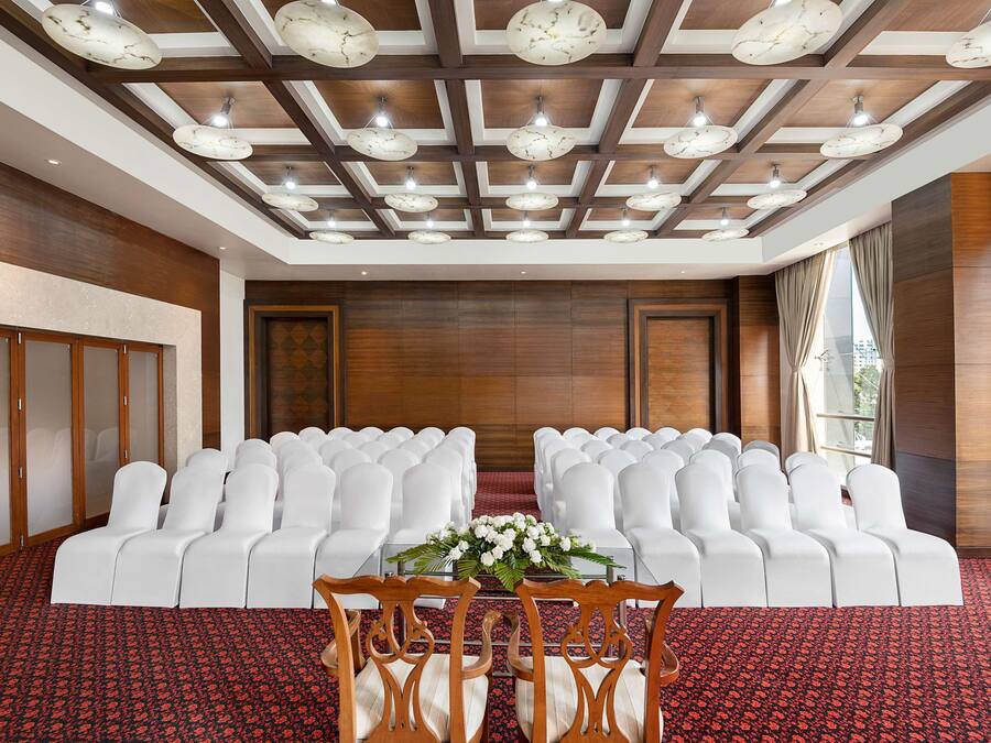 Une salle de conférence avec des chaises blanches disposées en rangées, un plancher en bois et un plafond orné d’un motif quadrillé de luminaires.