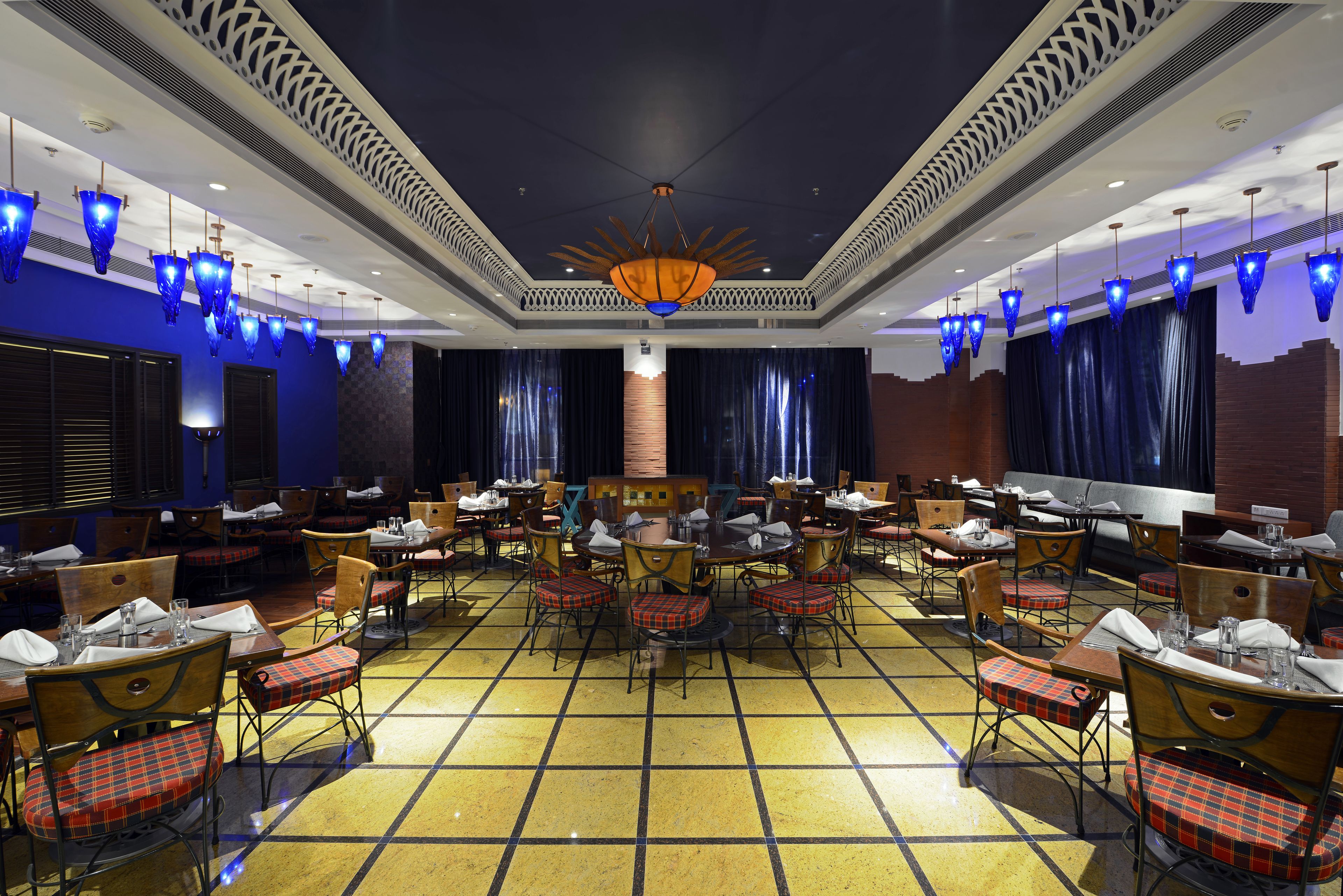 A spacious dining area with multiple tables and chairs, a central chandelier, and decorative blue lighting.