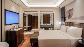Habitación de hotel moderna con una cama grande, un escritorio, un televisor y un baño visible a través de una puerta abierta.