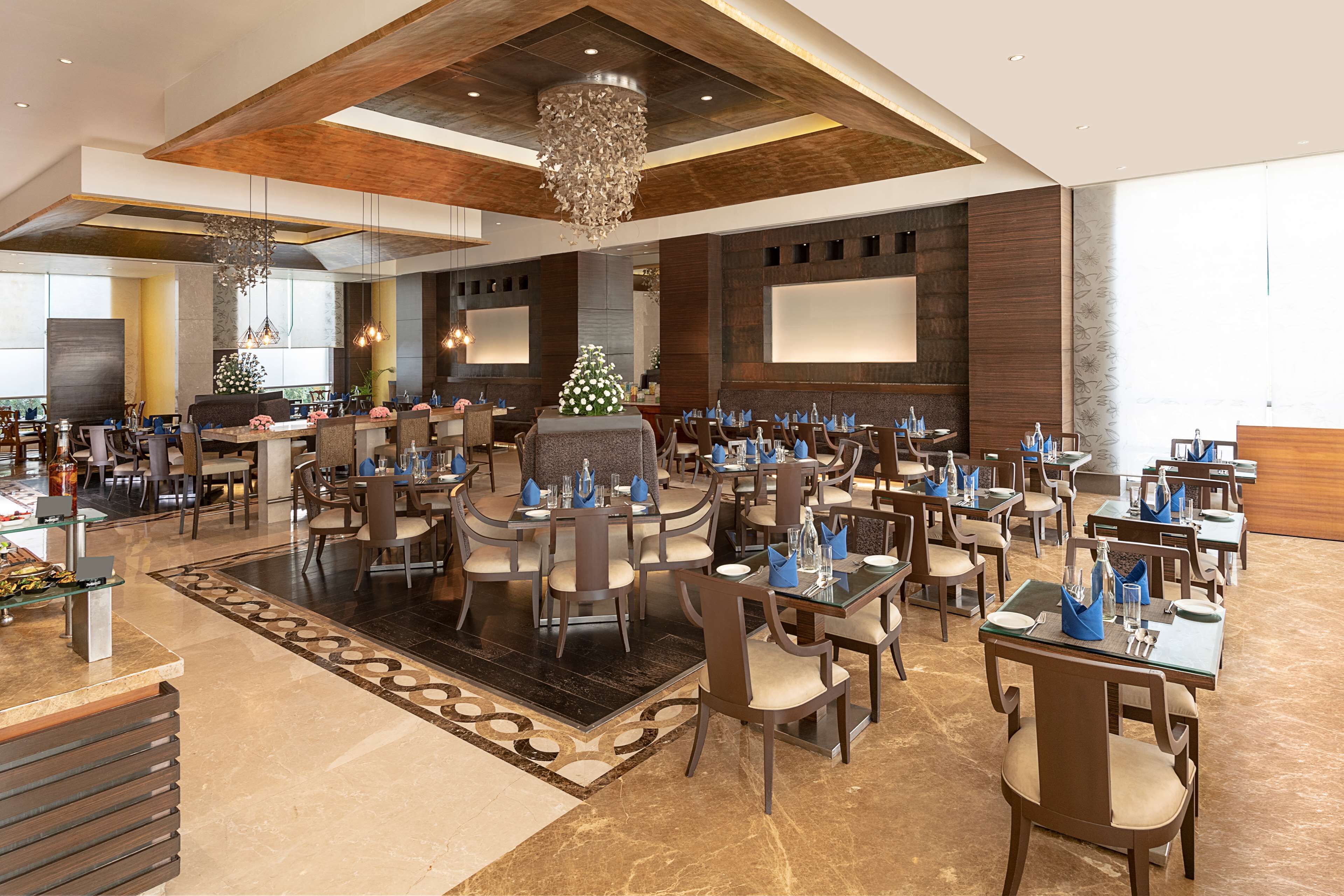 A spacious hotel lobby with multiple dining tables and chairs, a large chandelier, and a Christmas tree.