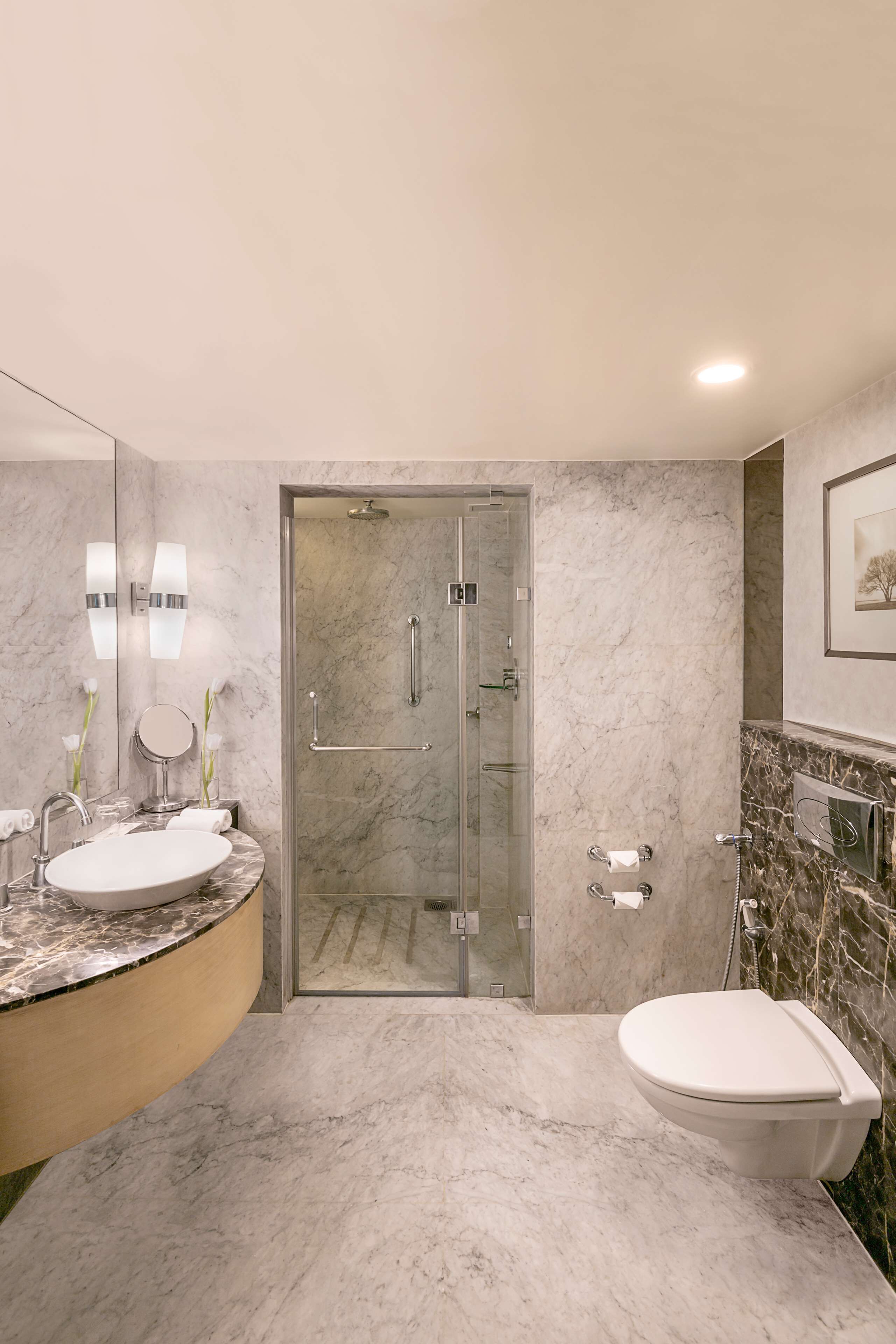 Un baño moderno con lavamanos de mármol, ducha con mampara de vidrio y un inodoro.