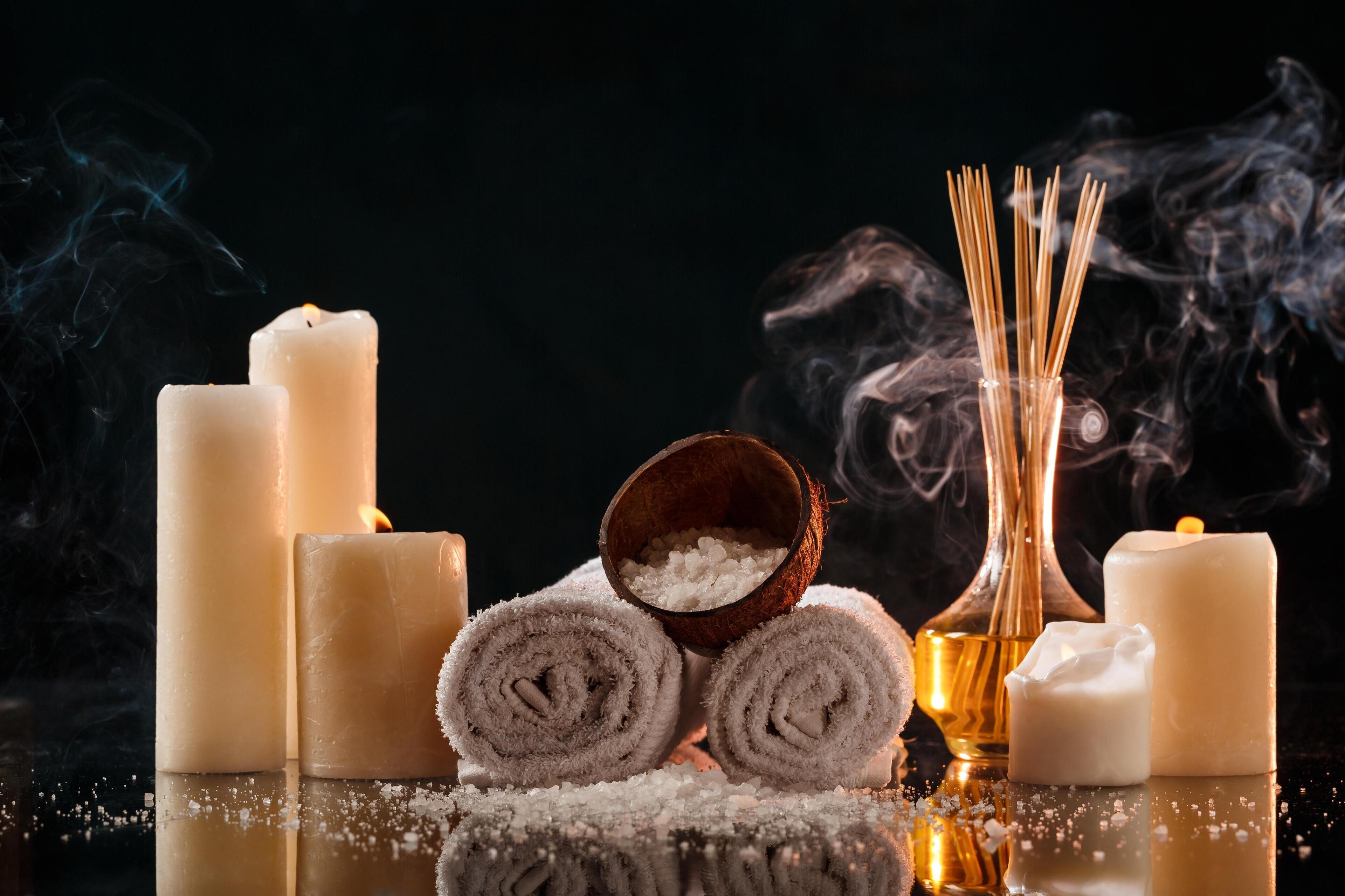Candles, rolled towels, and a bowl of salt on a reflective surface.