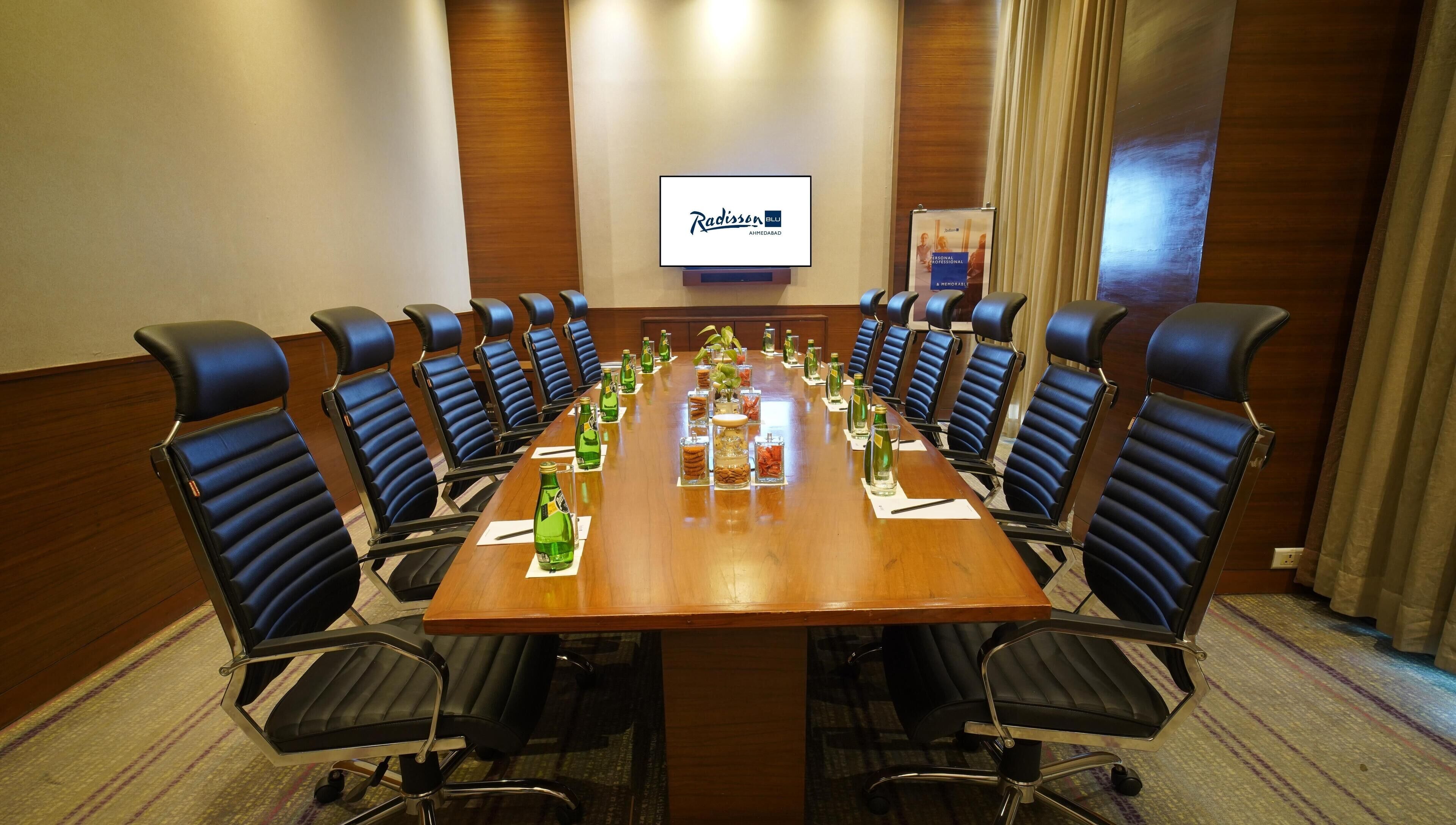 A conference room with a long table, 12 black chairs, and a Radisson Blu sign on the wall.