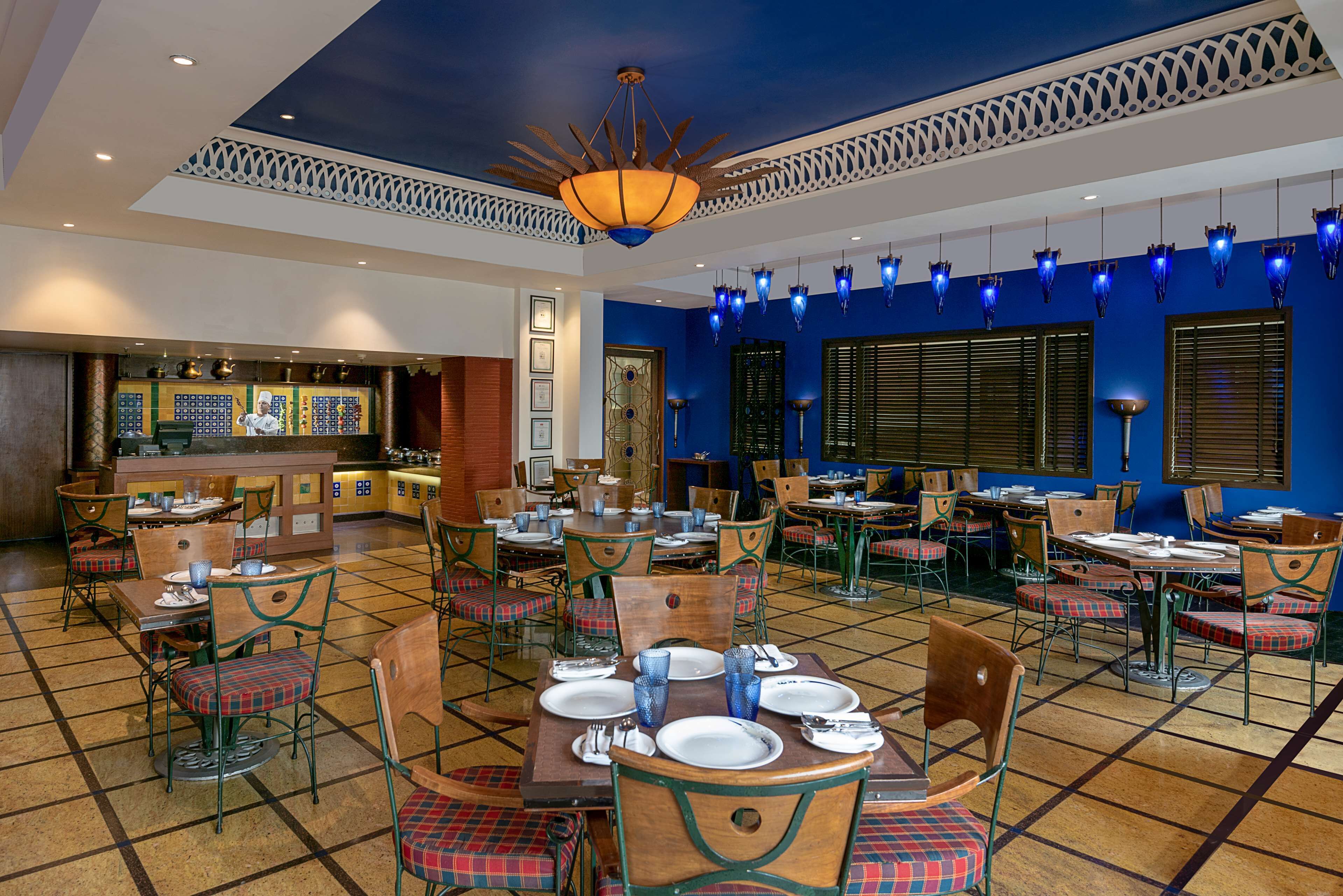 Un restaurante con una decoración en tonos azul y amarillo, que cuenta con una barra central, varias mesas con sillas y un techo decorativo.