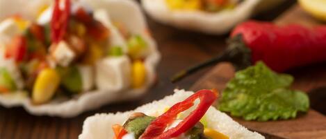 A close-up of a food dish with a variety of colorful ingredients, including corn, red peppers, and green vegetables, served in a paper cup.