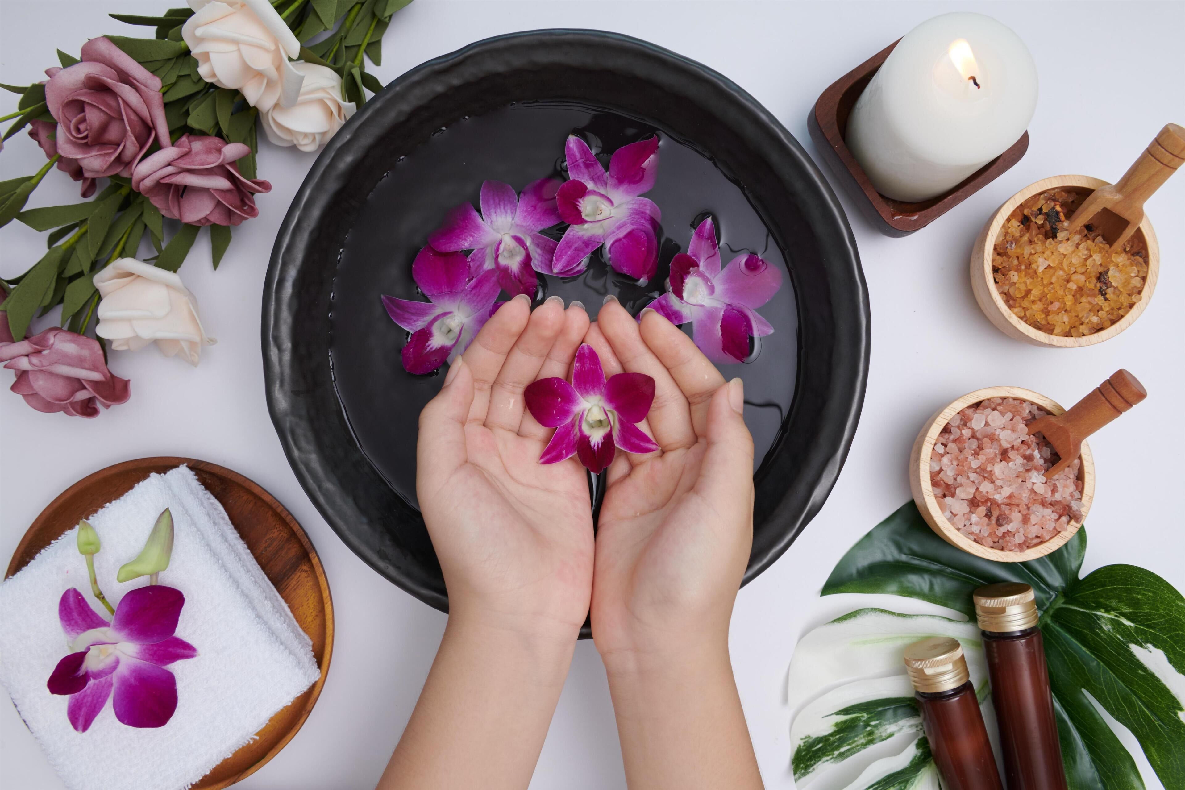 A spa setting with a black basin, pink and white flowers, a candle, and a wooden bowl with pink crystals.