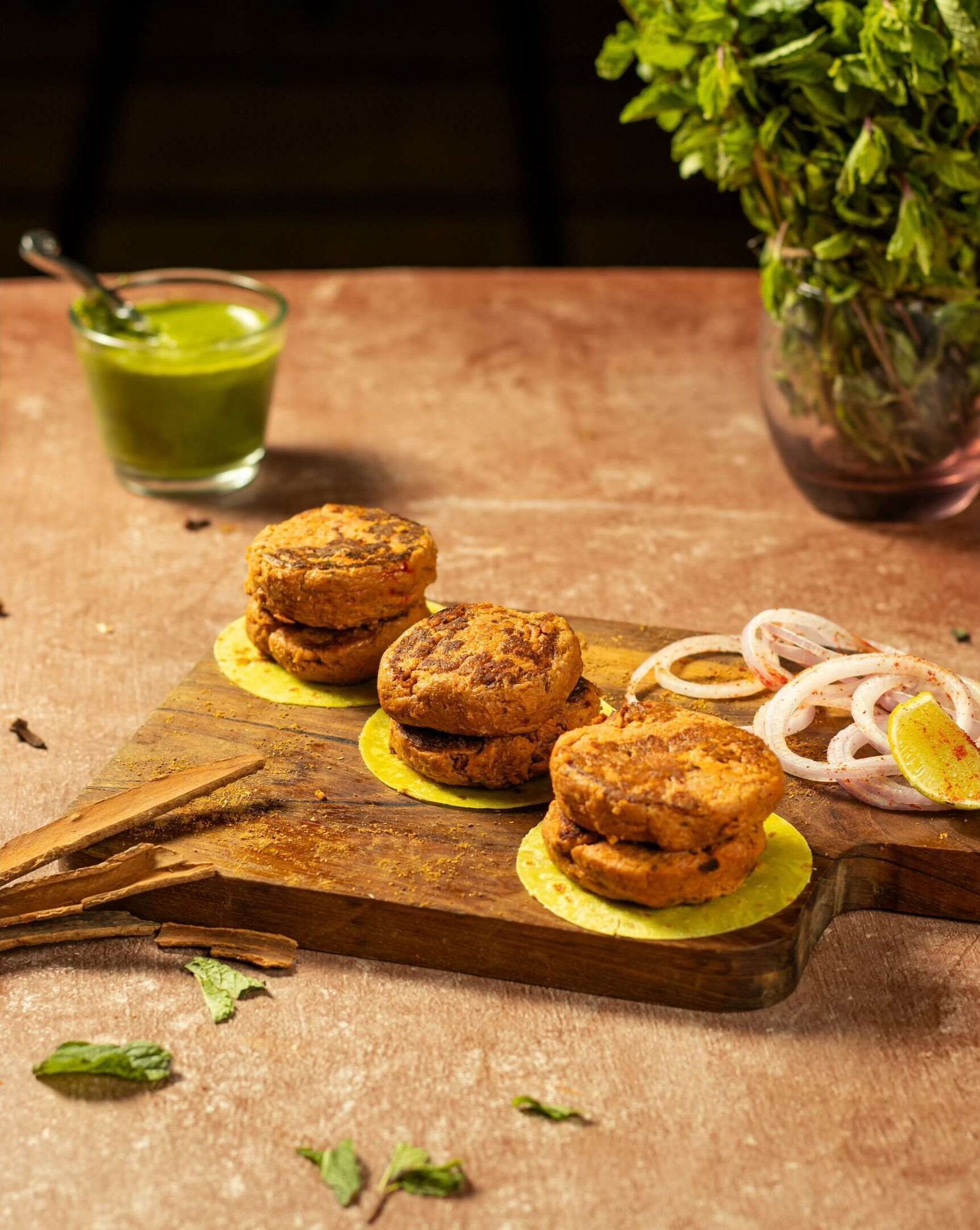 A wooden board with several food items, including what appears to be a type of cookie or pastry, and sliced onions, with a green drink and a potted plant in the background.