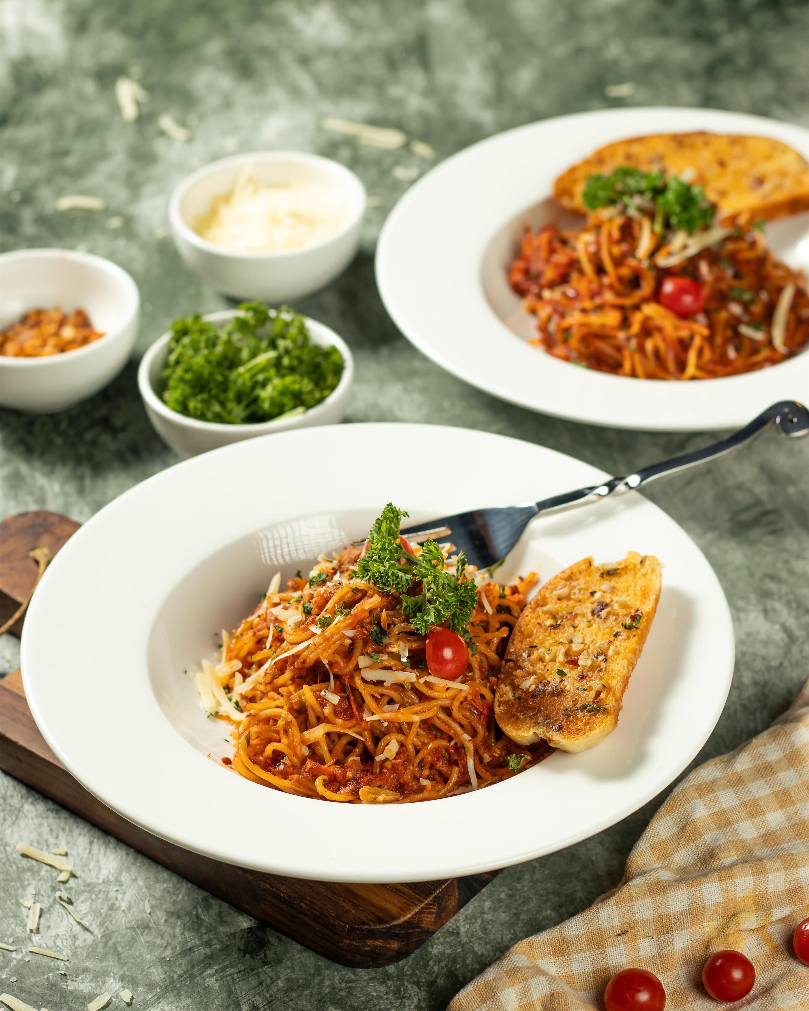 A plate of spaghetti with tomato sauce, garnished with parsley and cherry tomatoes, accompanied by a piece of toasted bread.