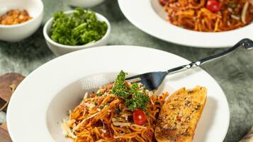 A plate of spaghetti with tomato sauce, garnished with parsley and cherry tomatoes, accompanied by a piece of toasted bread.