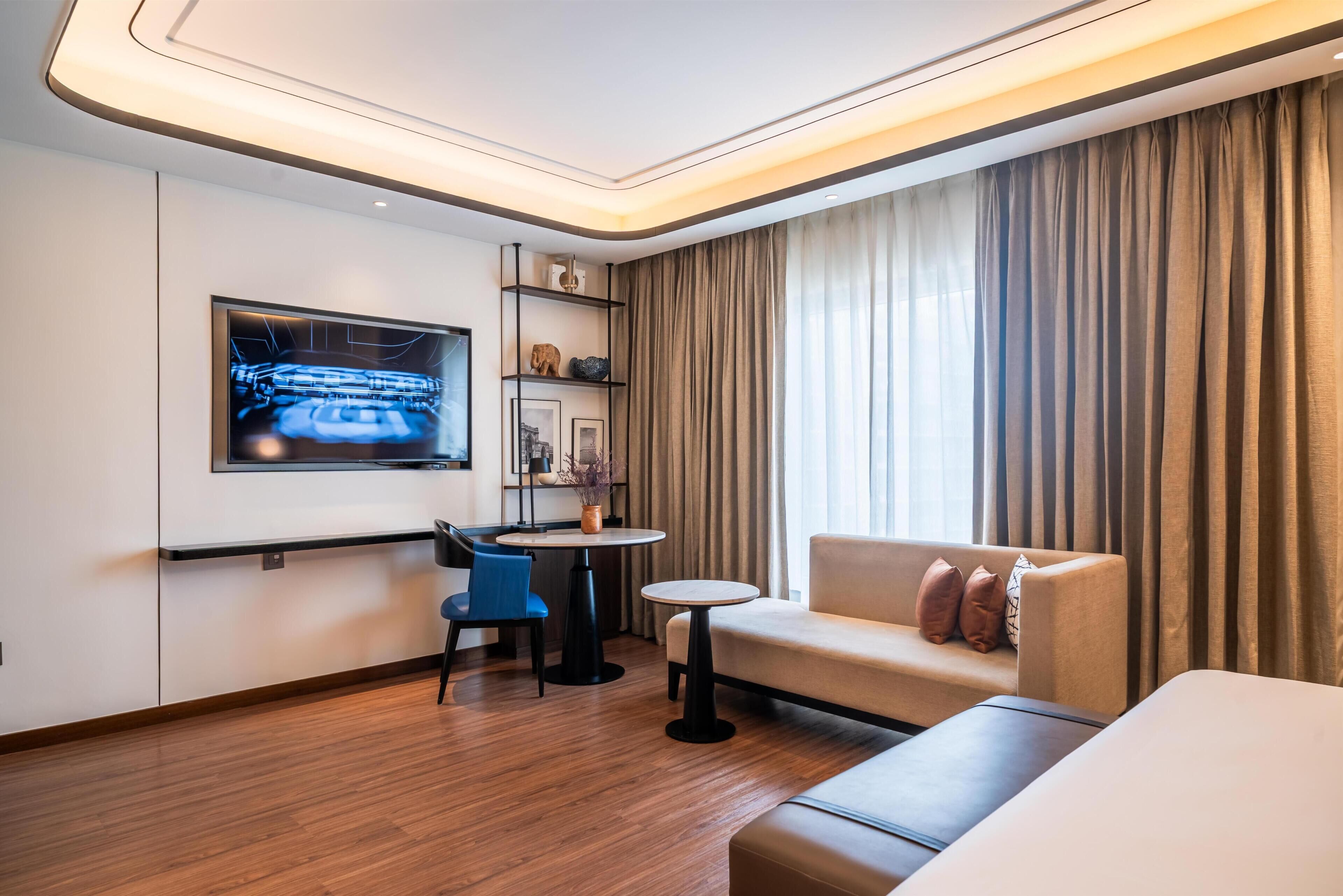 Una habitación de hotel moderna con televisi ón de pantalla plana, un sofá, una mesita y una silla.
