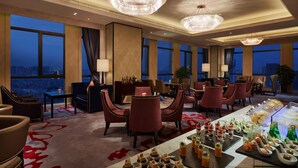 Un espacioso comedor de hotel con techos altos, grandes candelabros y vistas a la ciudad.