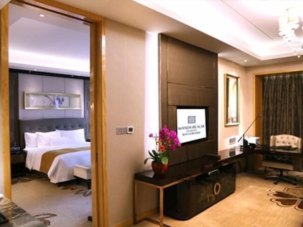Habitación de hotel con cama, televisor en la pared, escritorio con silla y un amplio ventanal con cortinas.