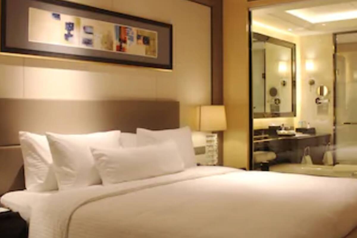 Ein Hotelzimmer mit einem großen Bett, einem Nachttisch, einer Lampe, einem Spiegel und einem gerahmten Kunstwerk an der Wand.