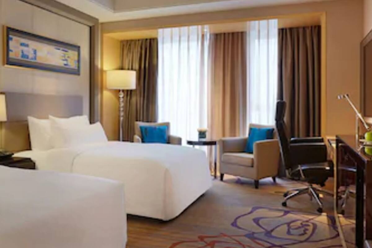 Ein Hotelzimmer mit zwei Betten, einem Schreibtisch, einem Stuhl, einer Lampe und Blick ins Freie.