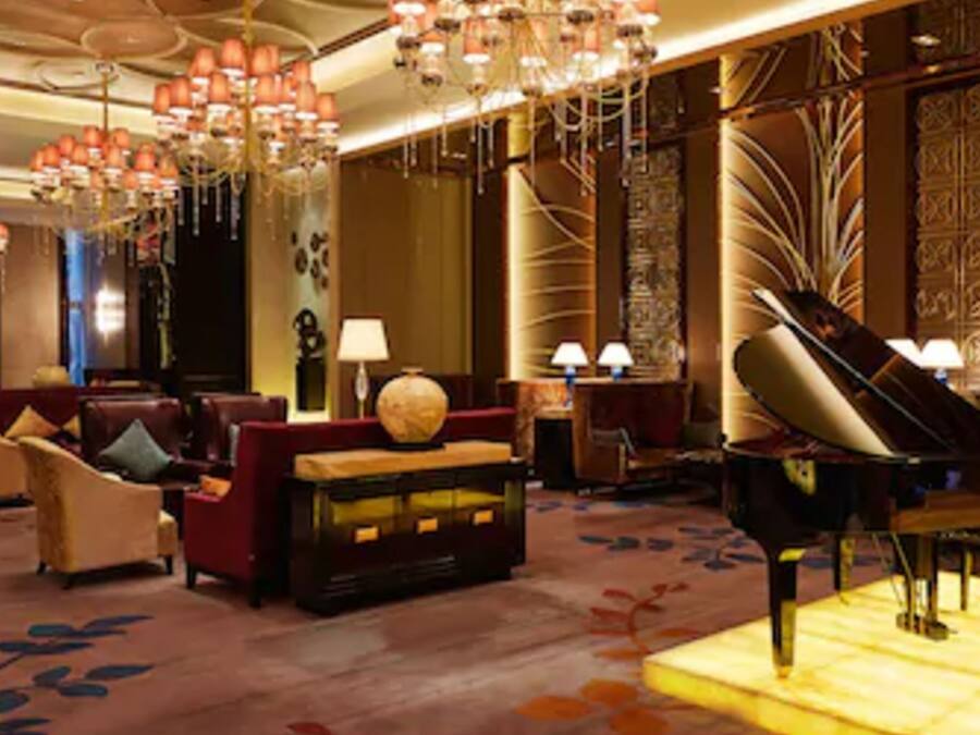 A luxurious lobby with a grand piano, plush seating, and ornate chandeliers.