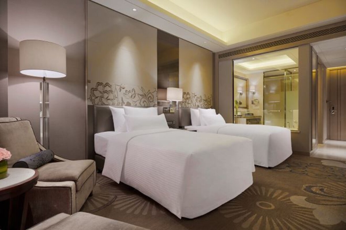 A hotel room with two beds, a sitting area with a chair and a table, and a large mirror.