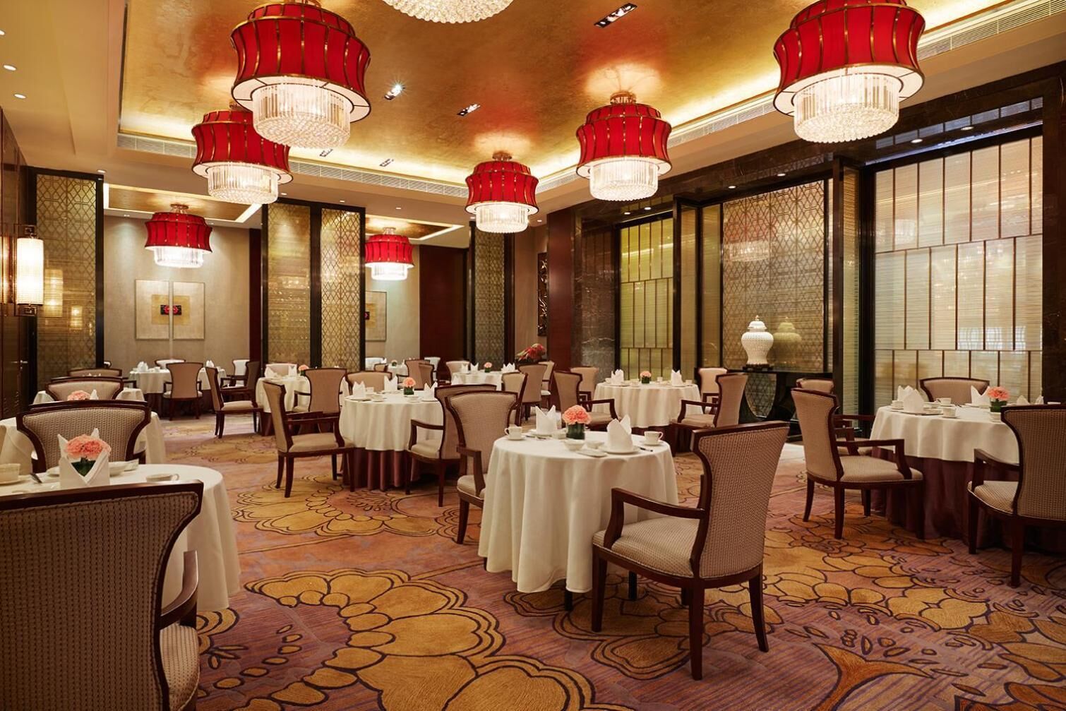 A restaurant with round tables, red chandeliers, and patterned carpet.