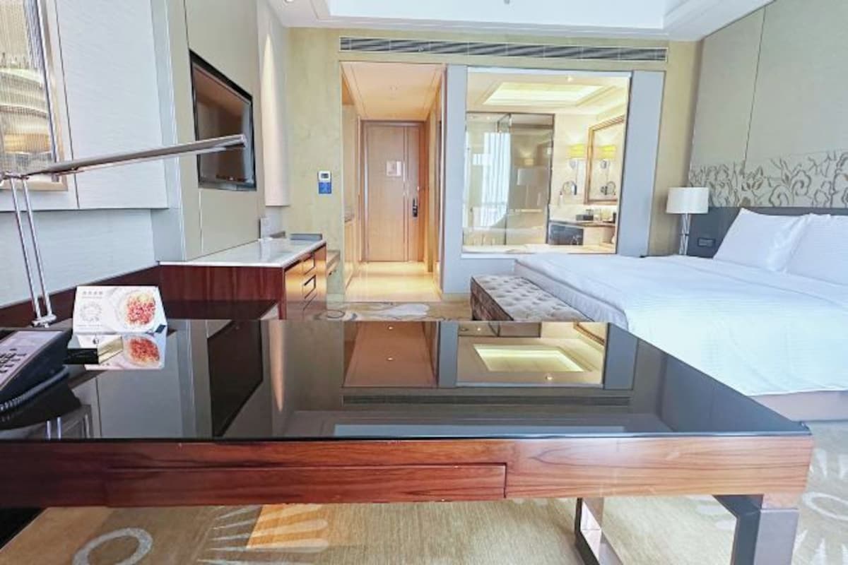 A hotel room with a glass-top desk, a bed, a bathroom, and a view of the city.