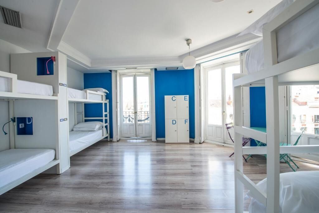 A dormitory room with bunk beds, a wardrobe, and a view of the city.