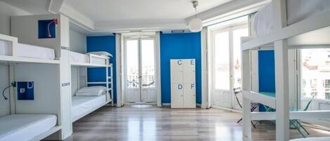 A dormitory room with bunk beds, a wardrobe, and a view of the city.