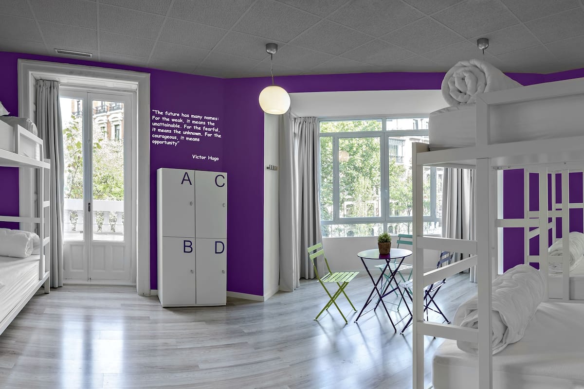 Une chambre d’hôtel moderne avec des lits superposés, un mur d’accent violet et une grande fenêtre donnant sur l’extérieur.